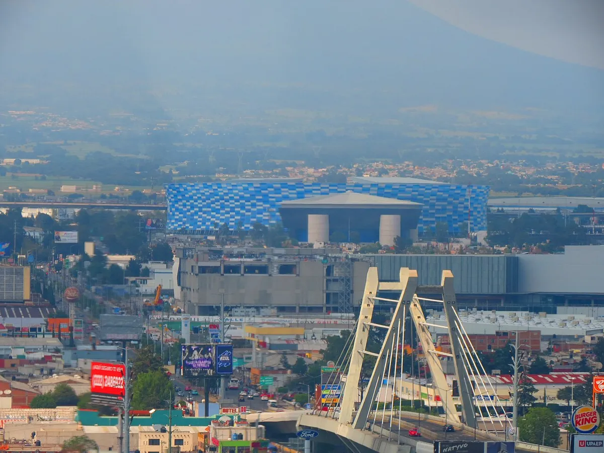 Estadio Cuauhtémoc and the blue ETFE facade visible from across Puebla with mountains in the background