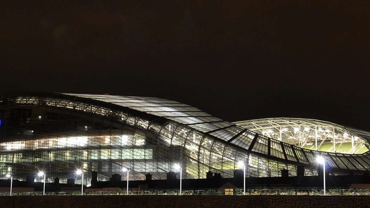 The Aviva Stadium in Dublin lit at night, its curved glass roof rising above the rooftops of Lansdowne Road