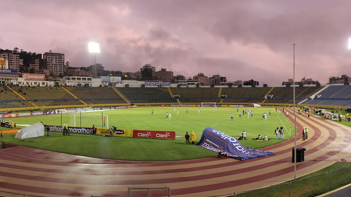 Estadio Olímpico Atahualpa in Quito, Ecuador, a high-altitude Andean stadium at dusk with the city and hills behind