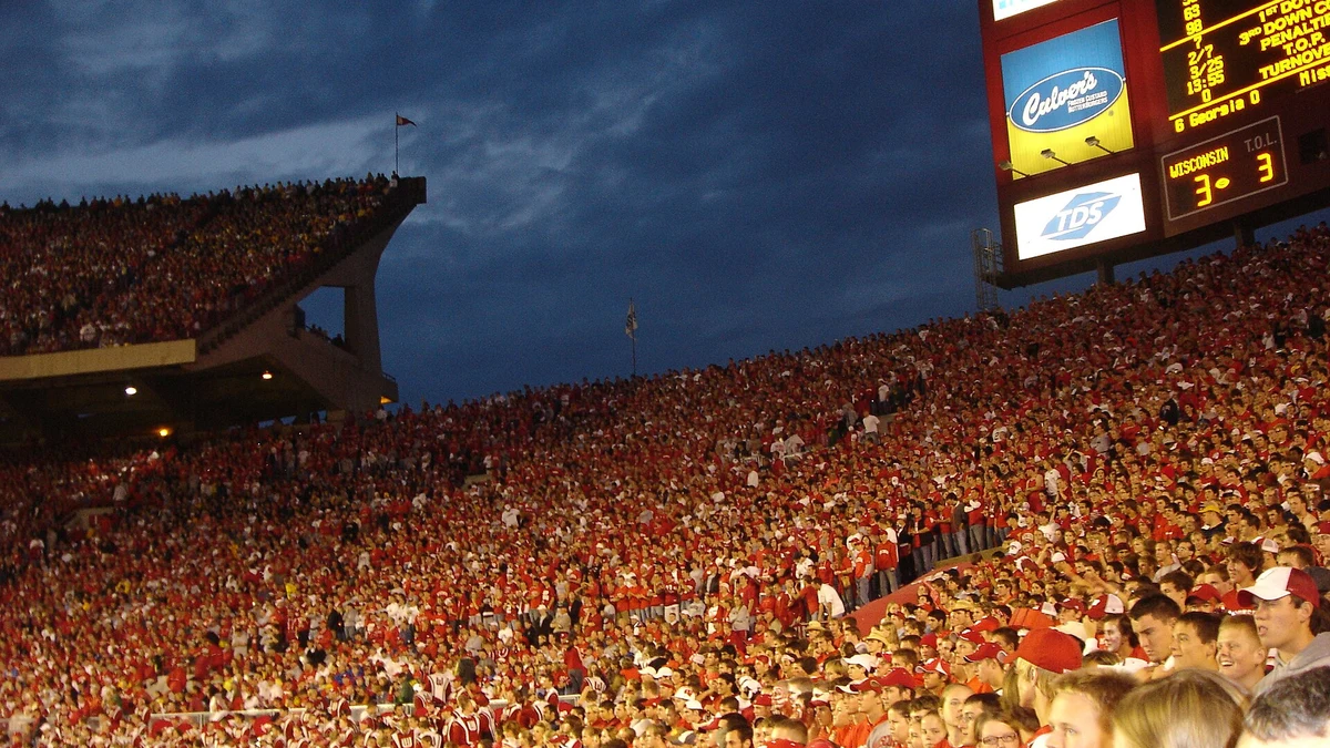 Camp Randall Stadium packed with Wisconsin students at dusk, the scoreboard lit above a full bowl