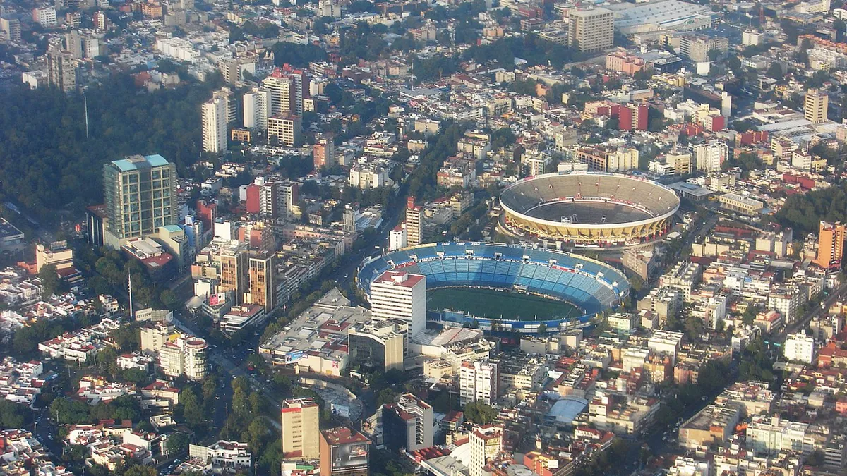 Aerial view of Mexico City's dense high-altitude sprawl, with a stadium and bullring visible among the rooftops