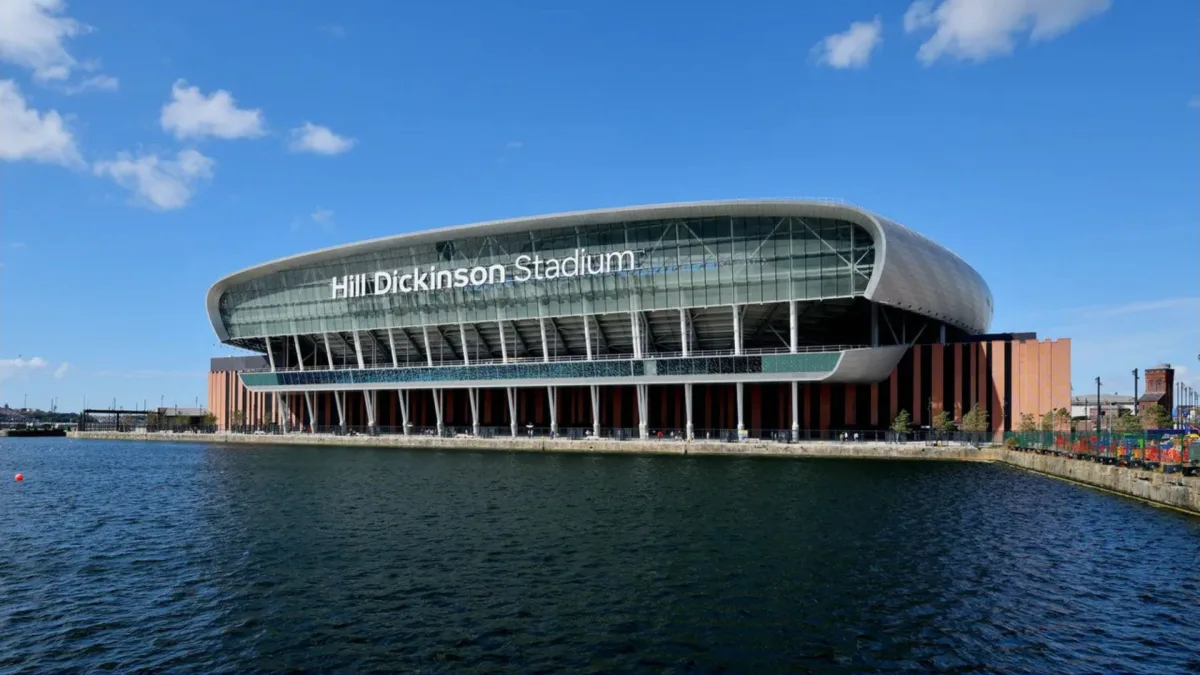 Hill Dickinson Stadium seen across the water at Bramley-Moore Dock, its name on the curved roof above red brick cladding