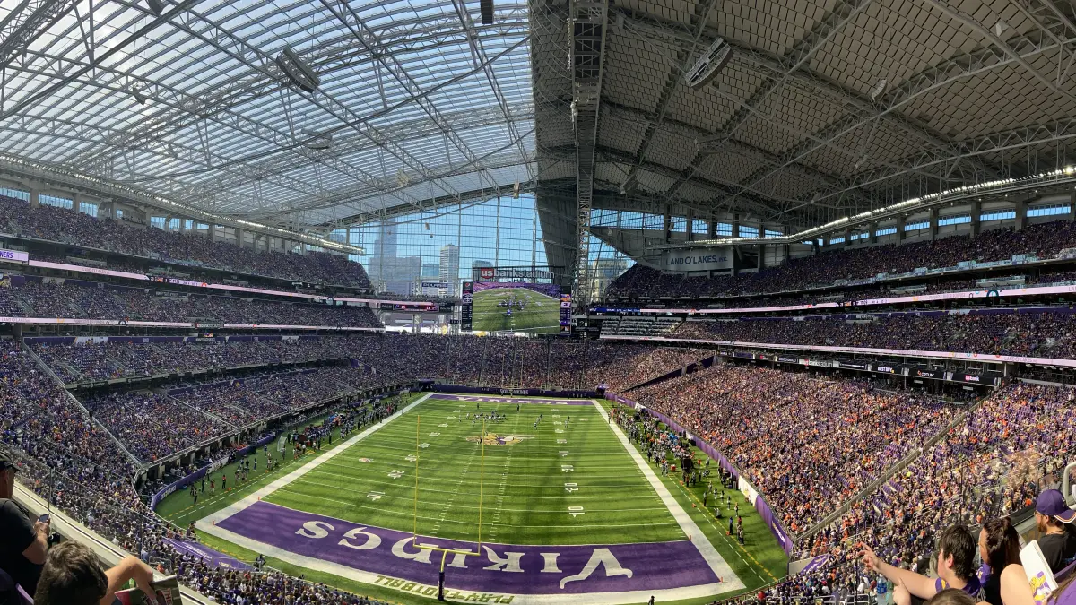 The interior of U.S. Bank Stadium in Minneapolis, showing the translucent ETFE roof over a packed bowl with the city skyline visible through the glass wall