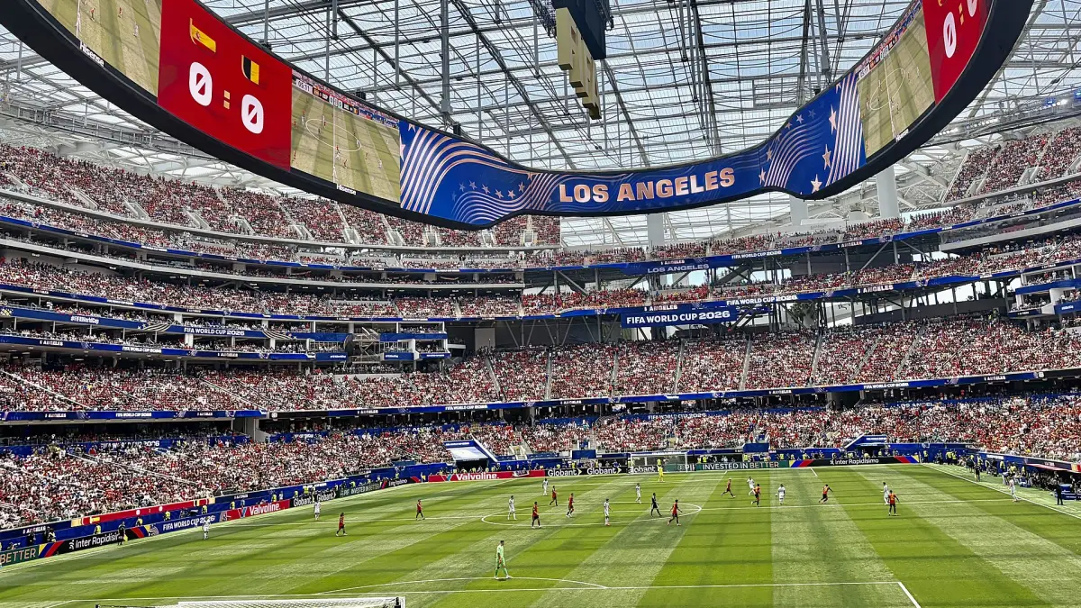 Inside SoFi Stadium in Los Angeles during a 2026 World Cup match, the natural grass pitch laid over the venue's artificial turf for the tournament