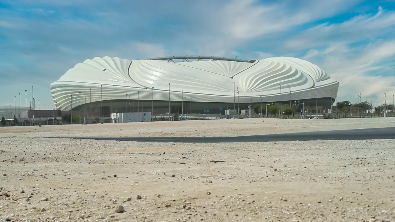 Al Janoub Stadium's white dhow-sail facade against a blue sky in Al Wakrah