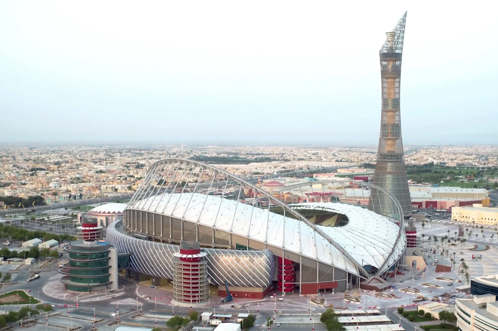 Aerial view of Khalifa International Stadium's twin arches and canopy beside the Torch Doha tower